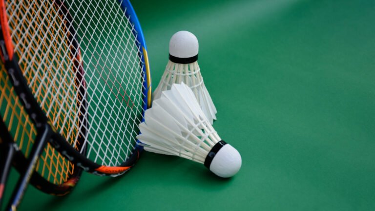 Cream white badminton shuttlecocks and rackets on green floor in indoor badminton court, copy space.